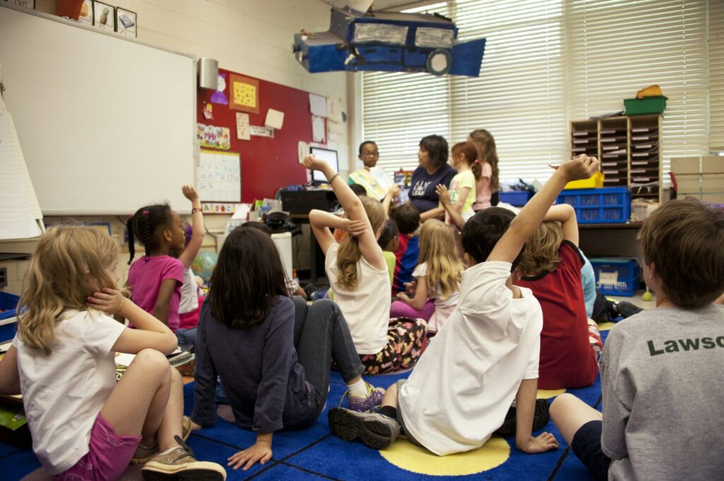 a photo of students sitting on the floor and raising their hands